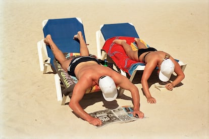 Una pareja trata de leer en una postura incómoda mientras toma el sol en una playa de Mallorca.