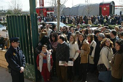 Una gran fila de personas se dirigen a votar en el barrio de El Pozo; al fondo, el tren en el que viajaban las víctimas del atentado.