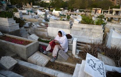 Una mujer paquistaní lee el Corán al lado de una tumba de sus parientes, en Karachi.