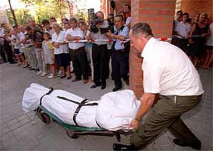 Los vecinos observan mientras un empleado de la funeraria saca de la vivienda de vallecas el cadáver de una de las mujeres tiroteadas.