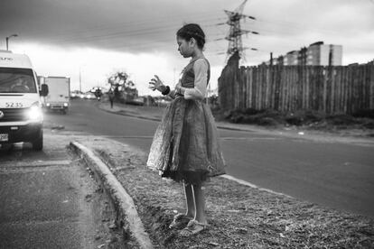 En mitad de una autopista en las calles de Bogotá, capital colombiana, una niña sostiene un vaso de plástico.
