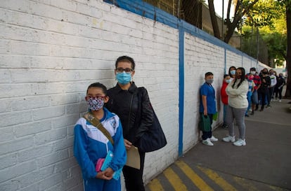 Los niños son acompañados por familiares mientras hacen fila para tomarse la temperatura antes de ingresar a una escuela durante la reanudación de las clases presenciales en la Ciudad de México.