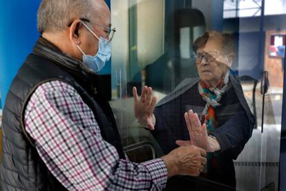 Una pareja se saluda a través de un cristal en la residencia de ancianos Ca n’Arnaus de Terrassa.