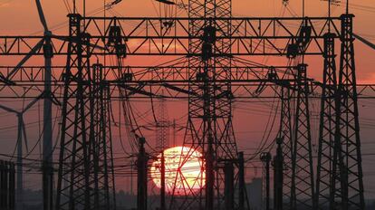 En la imagen, una puesta de sol junto al tendido eléctrico y unos molinos de viento (izq).