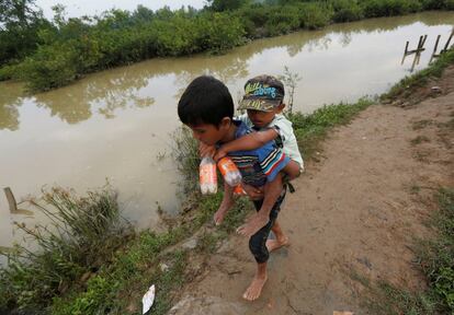 Un niño refugiado rohingya lleva a su hermano menor a la espalda mientras caminan después de cruzar el río Naf en la frontera entre Bangladés y Myanmar.