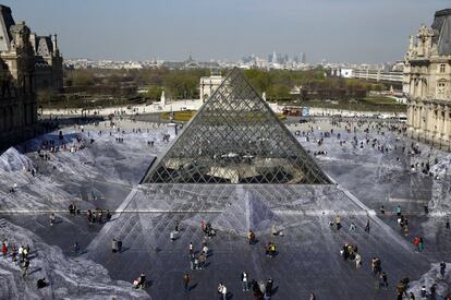 Un total de 400 voluntarios en equipos de 50 pasaron cuatro días pegando tiras de papel impreso en los adoquines del patio, creando un mosaico gigante alrededor de la pirámide. En la imagen, los turistas caminan sobre el gigantesco trabajo fotográfico de Jr.