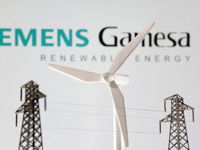 Miniaturas de un aerogenerador y dos torres eléctricas, con el fondo de Siemens Gamesa al fondo.