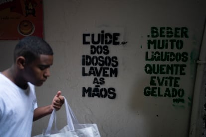 Um homem passa em frente a recados de conscientização sobre o coronavírus na Rocinha, Rio de Janeiro.