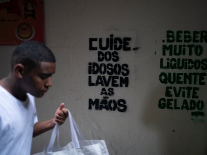 Um homem passa em frente a recados de conscientização sobre o coronavírus na Rocinha, Rio de Janeiro.