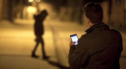 A man checks his cellphone as a young woman walks by.