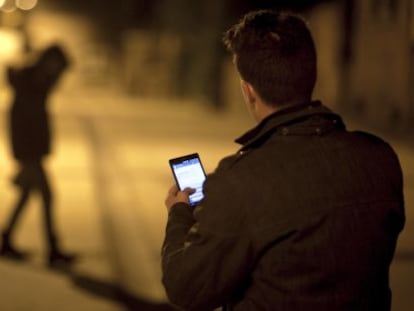 Um homem usa seu celular diante da silhueta de uma jovem.