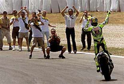 Valentino Rossi, conduciendo su moto de pie, saluda a un grupo de aficionados tras su triunfo.