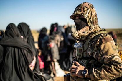 Un miembro de las fuerzas kurdas junto a un grupo de mujeres y niños tras abandonar Baghuz, el último bastión del ISIS.