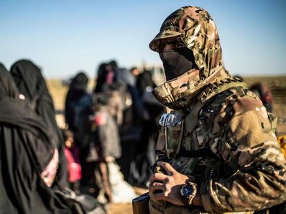 Un miembro de las fuerzas kurdas junto a un grupo de mujeres y niños tras abandonar Baghuz, el último bastión del ISIS.
