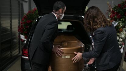Dos conductores introducen un féretro en el interior del vehículo fúnebre en Barcelona.