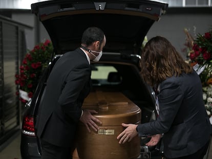 Dos conductores introducen un féretro en el interior del vehículo fúnebre en Barcelona.