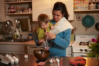 Una mujer cocina con su bebé en brazos.