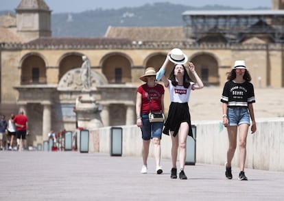 Varias personas intentan protegerse de la altas temperaturas a su paso por el puente romano de Córdoba.