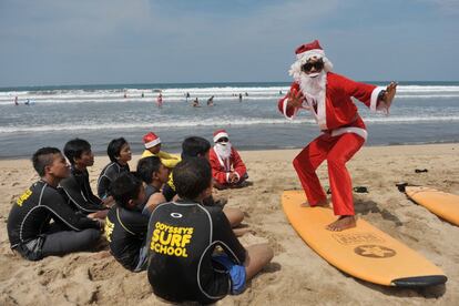 Un instructor de surf vestido de Papa Noel da una clase a niños huérfanos, en la playa de Kuta (Bali).