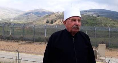 El líder espiritual druso Jad al Karim Nasser, ante la valla de separación con Siria en Majdal Shams. Al fondo, base militar siria en la Colina de los Gritos