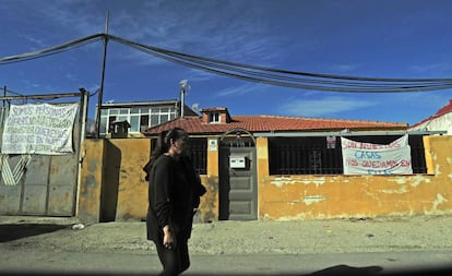 Una vecina de la Cañada Real pasea frente a algunas de las casas que tienen colgados carteles contra la previsión de realojo en sus fachadas.