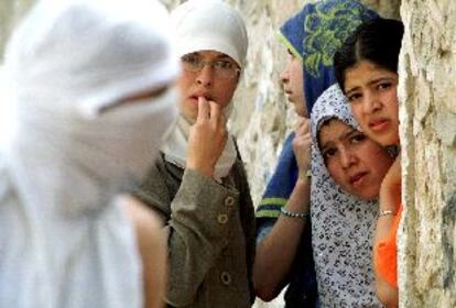 Un palestino encapuchado camina por delante de un grupo de mujeres refugiadas tras un muro durante los enfrentamientos de ayer en Jerusalén.