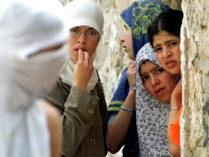 Un palestino encapuchado camina por delante de un grupo de mujeres refugiadas tras un muro durante los enfrentamientos de ayer en Jerusalén.