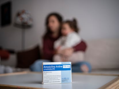 Una caja de amoxicilina en primer término, con una madre y su hija al fondo.