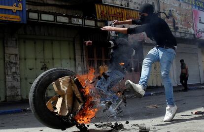 Un manifestante palestino patea un neumático en llamas durante los enfrentamientos con las tropas israelíes en Hebrón (Cisjordania).