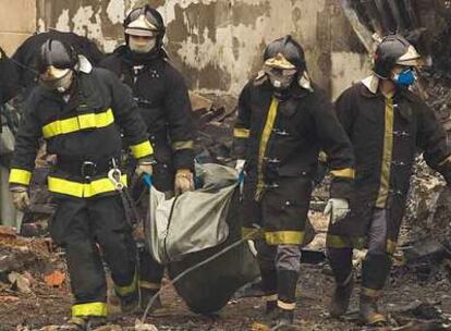 Cuatro bomberos trasladan los restos de una víctima del accidente aéreo.