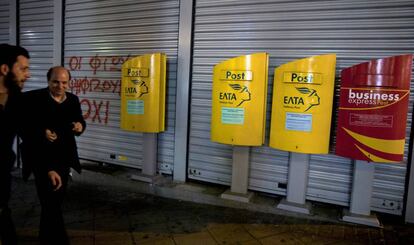 Dos hombres caminan frente a la oficina postal de Atenas, este lunes.