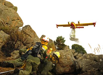 Integrantes de un retén forestal de extinción, se protegen entre las rocas de un hidroavión durante el incendio forestal en Collado Mediano ( Madrid). Unas 40.000 personas, entre profesionales y voluntarios, trabajan en España en labores de extinción de incendios.