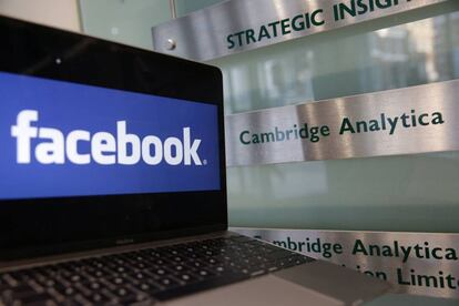 Un ordenador con el logo de Facebook junto a un cartel con el logo de Cambridge Analytica.
