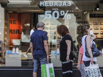 Varias personas observan objetivos del escaparate de una tienda con carteles indicativos de rebajas en Valencia.