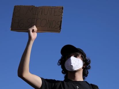 Um manifestante com uma máscara com os dizeres “não consigo respirar” segura um cartaz que faz menção aos 8 minutos e 46 segundos.