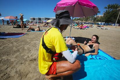 Un socorrista de la playa del Postiguet, en Alicante, informa a una ba?ista de las recomendaciones de no fumar. 