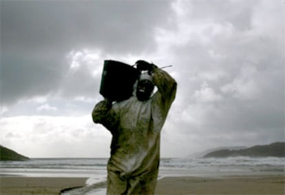 Un voluntario acarrea un capazo repleto de fuel en la playa de Estorde, en Cee (A Coruña).