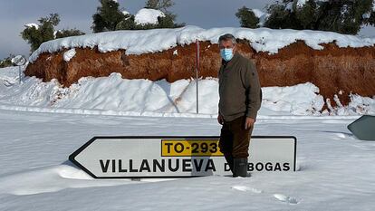 Un vecino de Villanueva de Bogas (Toledo) frente al rótulo de acceso al pueblo, semicubierto de nieve.