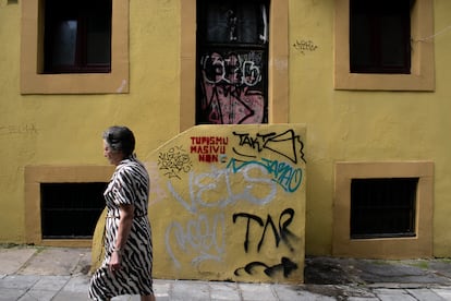 Una vecina del barrio gijonés de Cimadevilla pasea por la calle Atocha frente a unas pintadas contra el turismo masivo escritas en asturiano el 18 de julio.