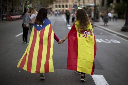 Dos niñas pasean por Barcelona, una con la estelada y la otra con la bandera de España.