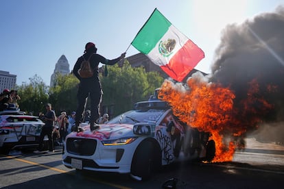 Tercer día de protestas en Los Ángeles contra redadas de ICE moviliza a cientos de personas 2 Un manifestante ondea una bandera mexicana sobre un taxi Waymo en llamas, este domingo frente al centro de detención metropolitano del centro de Los Ángeles.