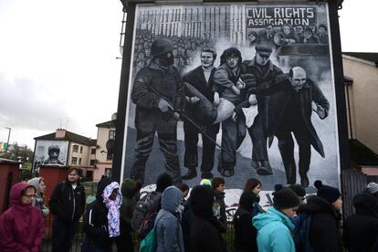 Turistas caminan delante de un mural que muestra al sacerdote Edward Daly ondeando una pañuelo ensangrentado mientras trasladan a Jackie Duddy, una de las víctimas del Domingo Sangriento. La fiscalía de Irlanda del Norte anunció este jueves que ha presentado cargos contra un exsoldado del Ejército británico por su presunta implicación en la muerte de dos civiles en el llamado Domingo Sangriento.