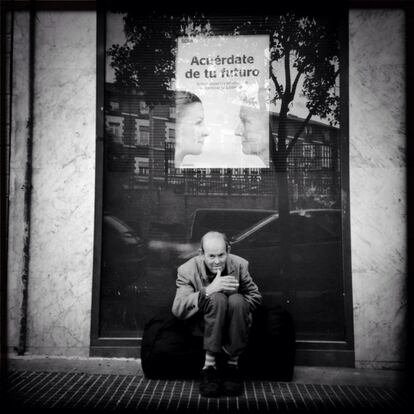 29-11-2014. Un hombre sentado bajo un cartel con la publicidad de un banco.