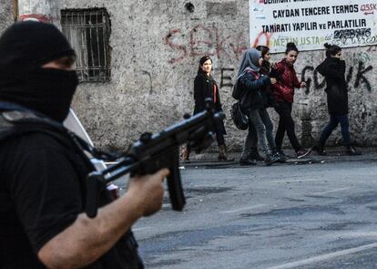 Un grupo de jóvenes camina por la calle en Diyarbakir (Turquía) mientras un policía sostiene un rifle de asalto durante las protestas contra los toque de queda impuestos por el Gobierno.