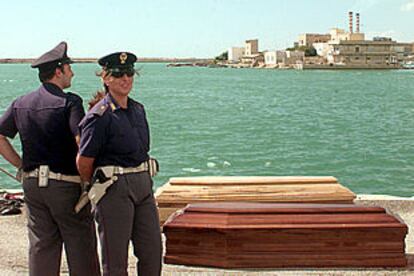 Dos policías italianos permanecen junto a los ataúdes de varios de los inmigrantes fallecidos en el naufragio. PLANO GENERAL - ESCENA