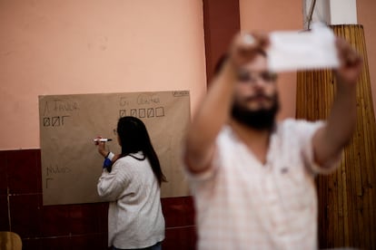 Un funcionario escribe el número de votos mientras otro tiene una papeleta, después del cierre de las urnas.