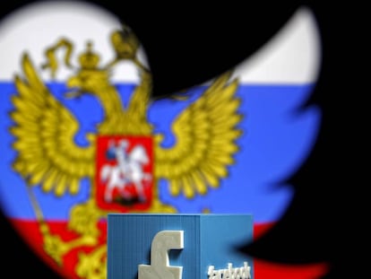 Una bandera rusa y un logo de Facebook vistos a través de un agujero con el logo de Twitter.