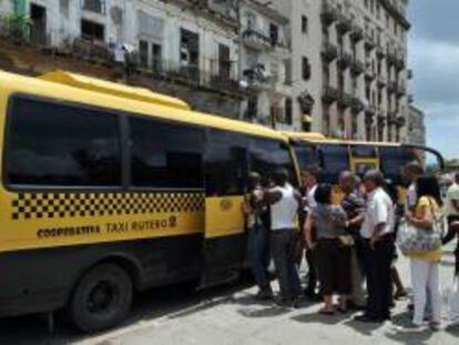 Varias personas hacen fila para subir a un ómnibus de una cooperativa de taxis colectivos en La Habana (Cuba).