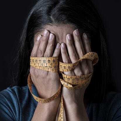 close up hands wrapped in tailor measure tape covering face of young depressed and worried girl suffering anorexia or bulimia nutrition disorder on black background obsessed with diet and overweight