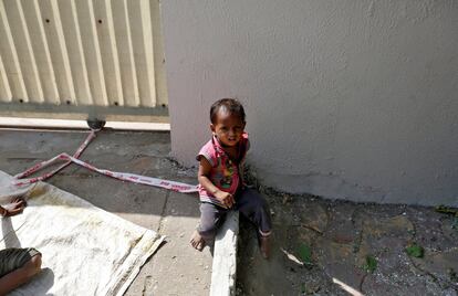 Barrier tape is tied around 15-month-old Shivani's ankle to prevent her from running away, while her mother Sarta Kalara works at a construction site nearby, in Ahmedabad, India, April 20, 2016. Kalara says she has no option but to tether her daughter Shivani to a stone despite her crying, while she and her husband work for 250 rupees ($3.8) each a shift digging holes for electricity cables in the city of Ahmedabad. There are about 40 million construction workers in India, at least one in five of them women, and the majority poor migrants who shift from site to site, building infrastructure for India's booming cities. Across the country it is not uncommon to see young children rolling in the sand and mud as their parents carry bricks or dig for new roads or luxury houses. REUTERS/Amit Dave       SEARCH "TIED TODDLER" FOR THIS STORY. SEARCH "THE WIDER IMAGE" FOR ALL STORIES